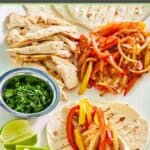 Grilled chicken fajitas, flour tortillas, fresh cilantro, and lime wedges.
