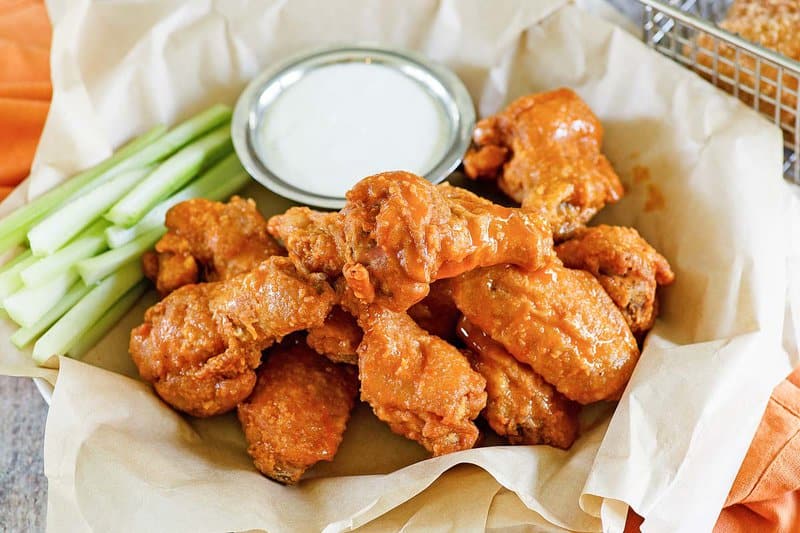 Copycat Hooters wings, celery sticks, and a cup of dipping sauce in a serving basket.