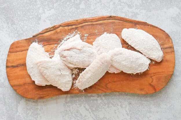 Breaded raw chicken wings on a wood board.