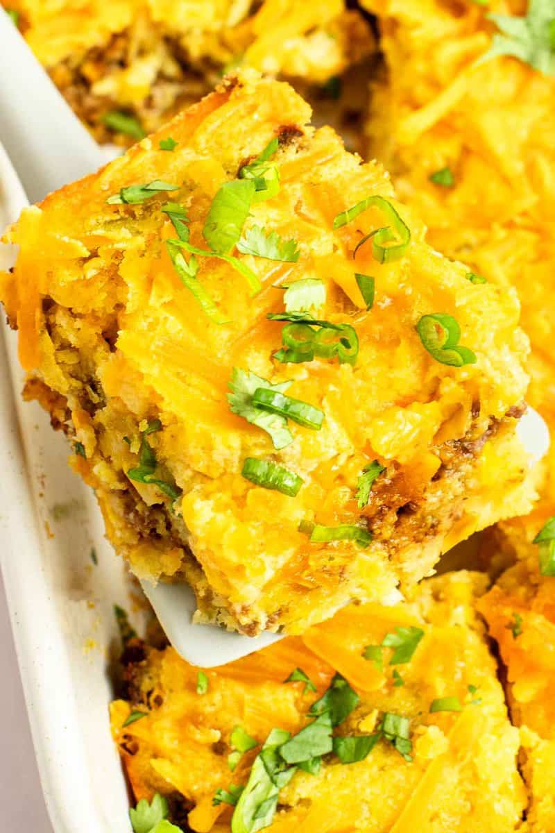 Mexican cornbread casserole slice on a spatula held over the dish.