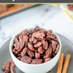 Homemade spiced pecans in a bowl and cinnamon sticks beside it.