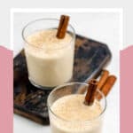 Two glasses of spiked eggnog garnished with cinnamon sticks.