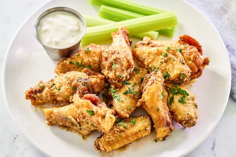 Copycat Wingstop garlic parmesan wings, celery sticks, and dipping sauce on a plate.
