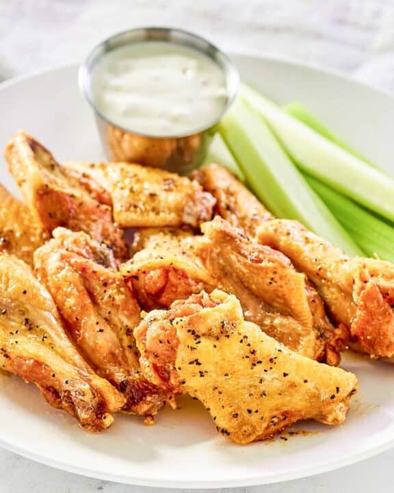 Copycat Wingstop lemon pepper wings, celery, and dipping sauce on a plate.