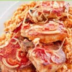 Baked pork chops with rice, onions, and tomato sauce on a platter.