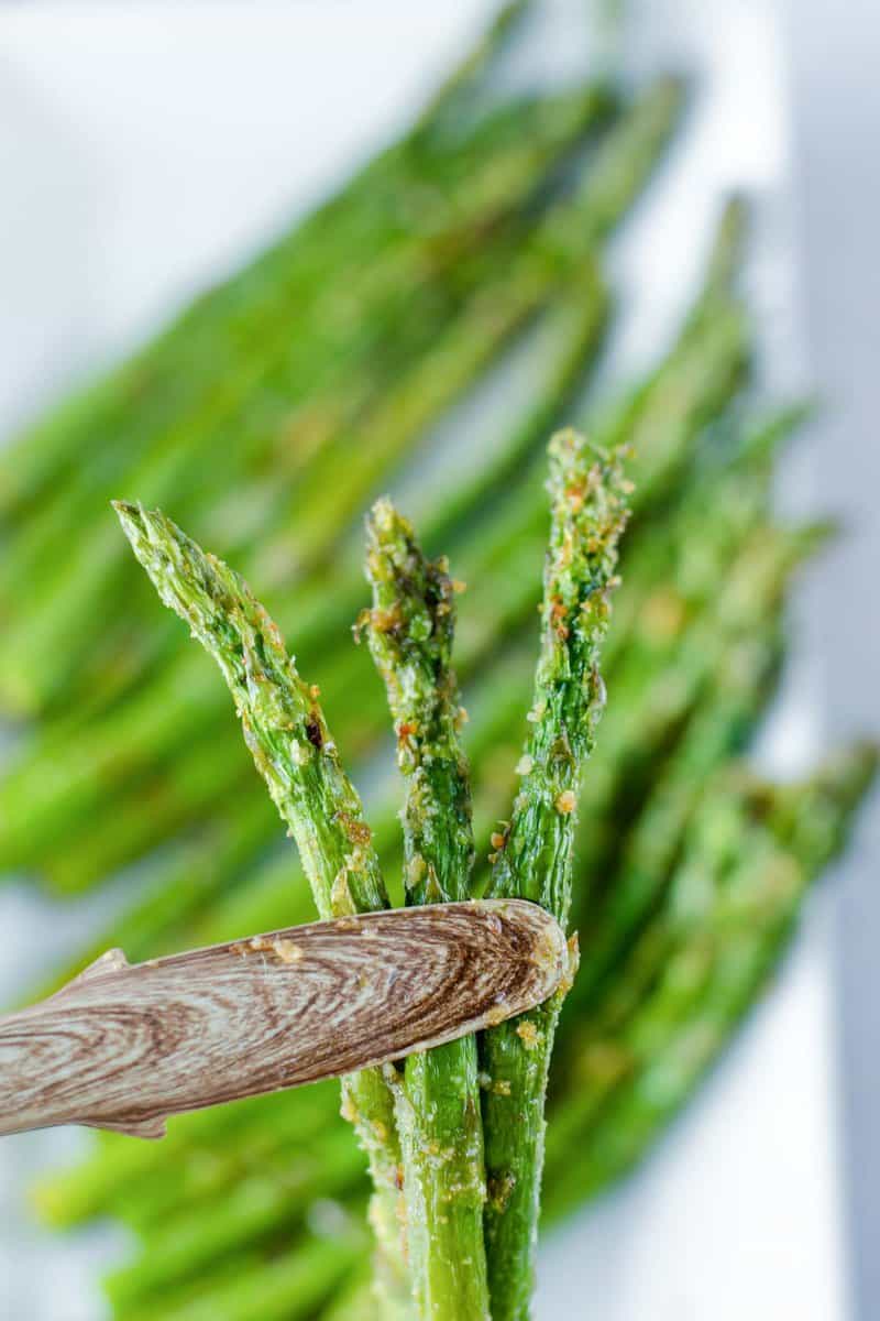 Wood tongs holding three air fried asparagus spears.
