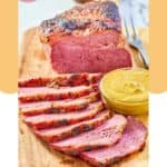 Baked corned beef on a wood carving board and a bowl of mustard.