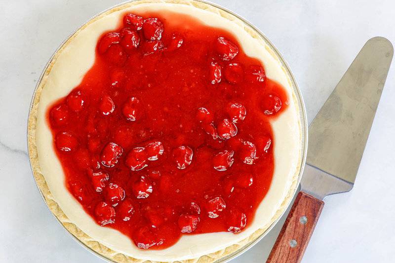 A whole cherry cream cheese pie and a pie server.