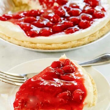 Slice of cherry cream cheese pie on a plate and the pie behind it.
