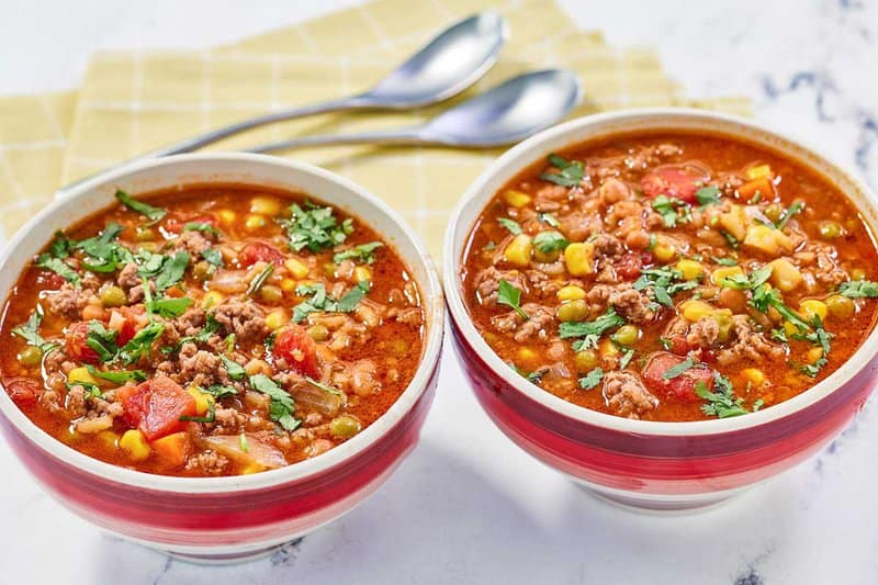 Two bowls of cowboy soup and two spoons behind them.