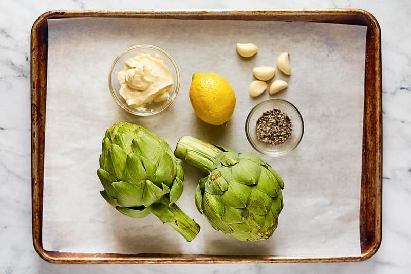 Grilled artichokes and garlic aioli ingredients on a tray.