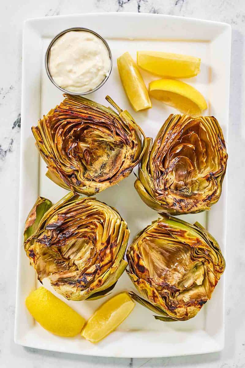 Grilled artichokes, garlic aioli, and lemon wedges on a platter.