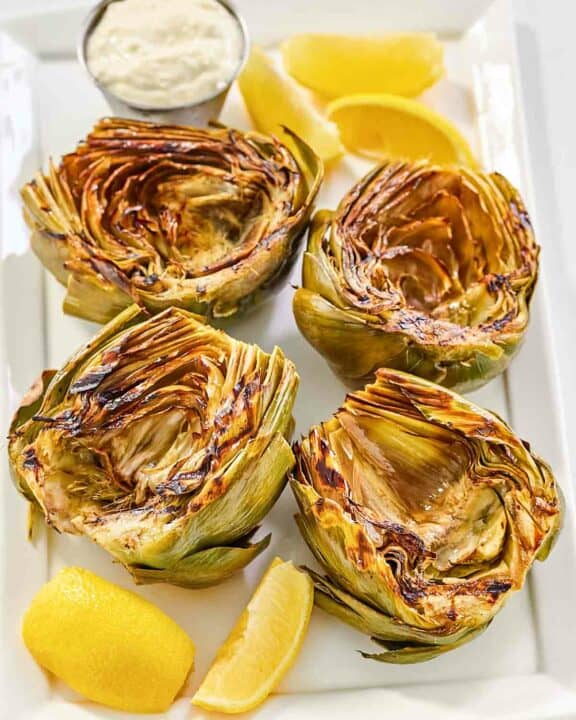 Grilled artichokes, garlic aioli, and lemon wedges on a platter.