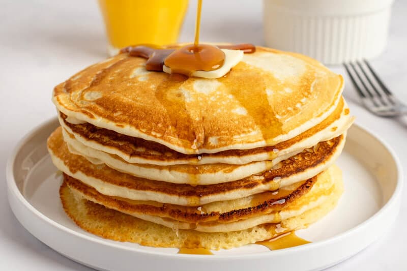 A stack of copycat IHOP buttermilk pancakes with butter and syrup being poured on them.