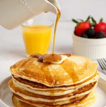 Pouring syrup over copycat IHOP buttermilk pancakes on a plate.