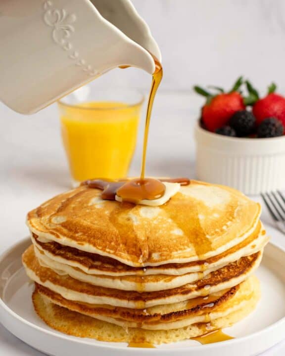 Pouring syrup over copycat IHOP buttermilk pancakes on a plate.