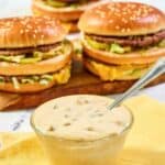 Homemade McDonald's big mac sauce in a bowl and big mac burgers behind it.