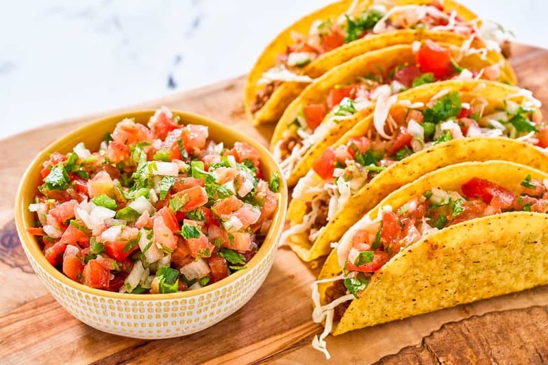 A bowl of copycat Applebee's pico de gallo next to tacos.
