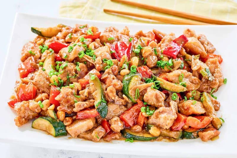Copycat Panda Express kung pao chicken on a plate and chopsticks behind it.