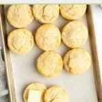 Homemade freezer biscuits on a baking sheet and one cut in half with butter on it.