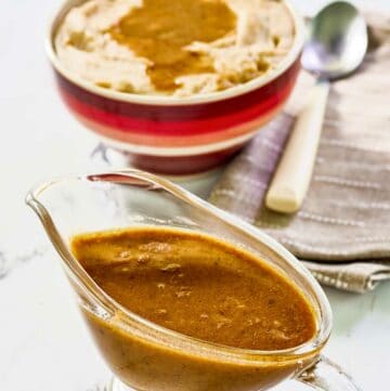 Copycat KFC gravy in a gravy boat and on top of mashed potatoes.