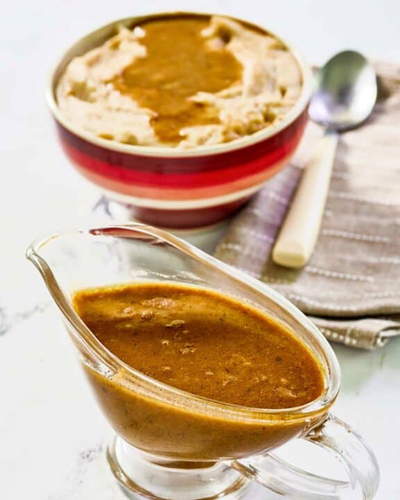 Copycat KFC gravy in a gravy boat and on top of mashed potatoes.