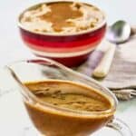 Homemade KFC gravy in a glass gravy boat and over mashed potatoes.