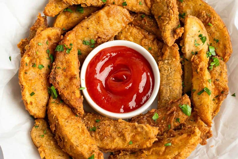 Copycat KFC potato wedges around a cup of ketchup.