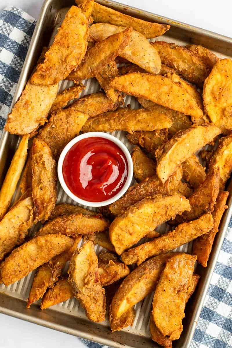Copycat KFC potato wedges and ketchup on a baking sheet.