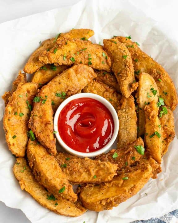 Copycat KFC potato wedges and ketchup in a serving bowl lined with parchment.