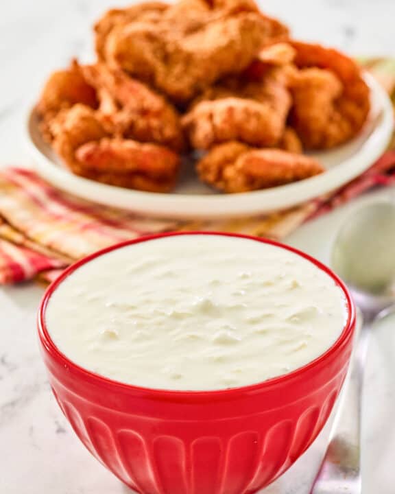 A bowl of copycat Red Lobster pina colada coconut shrimp sauce and coconut shrimp behind it.