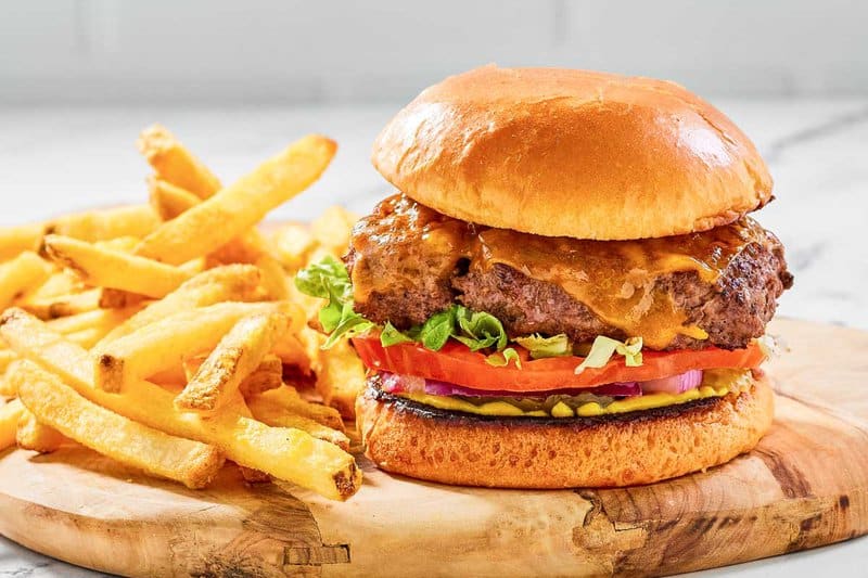 Copycat Chili's oldtimer burger with cheese and French fries on a wood board.