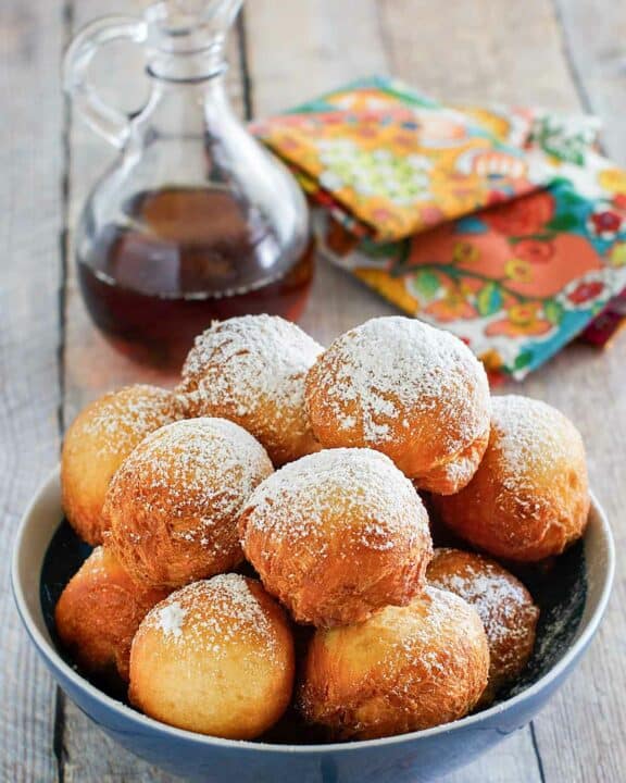 Copycat Denny's pancake puppies in a bowl and a bottle of syrup.