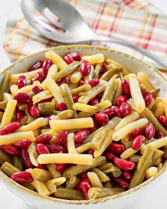 Grandma's three bean salad in a serving bowl and a slotted spoon on a napkin.