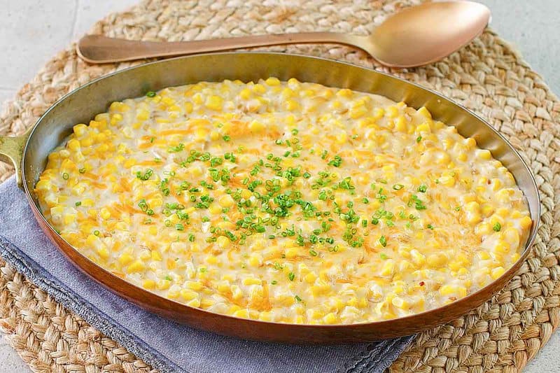 Cheesy creamed corn in a skillet and a serving spoon next to it.