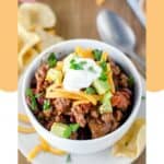 A bowl of chili topped with cheese, avocado, and sour cream.