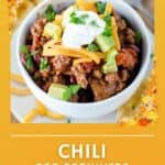 A bowl of chili topped with sour cream, cheese, and avocado.