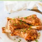 Roasted turkey legs on a plate on top of a wood board.