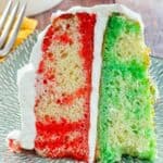 A slice of red and green jello poke cake with cool whip frosting.