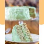 Pistachio cake slice on a plate and the cake on a cake stand.