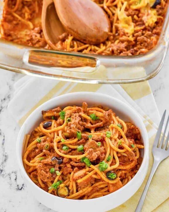 Taco spaghetti casserole in a baking dish and a serving in a bowl.