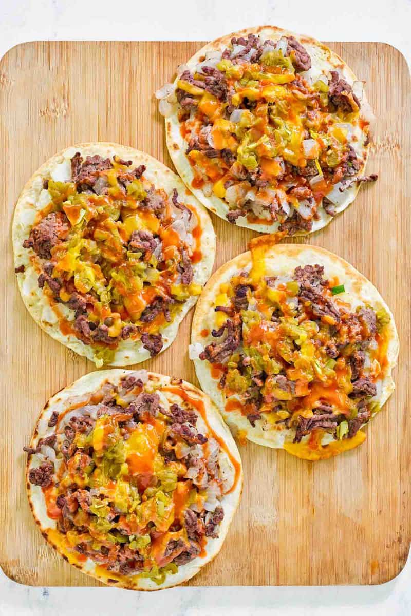Four copycat taco villa mexican pizza things on a wood cutting board.