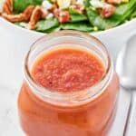 Copycat Bennigan's hot bacon dressing in a jar and a salad behind it.