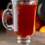 Homemade wassail in a mug on a wood surface.