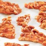 Microwave peanut brittle pieces scattered on parchment paper.