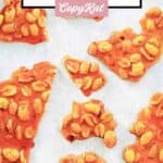 Several pieces of homemade peanut brittle scattered on parchment paper.