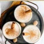 Three glasses of milk punch with cinnamon sticks in them.