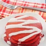 Homemade red velvet pancakes on a plate and a fork next to it.