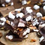 Pieces of homemade rocky road candy with walnuts stacked on a wood board.