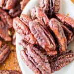 Homemade spiced pecans on a large spoon over the pecans on a wood board.